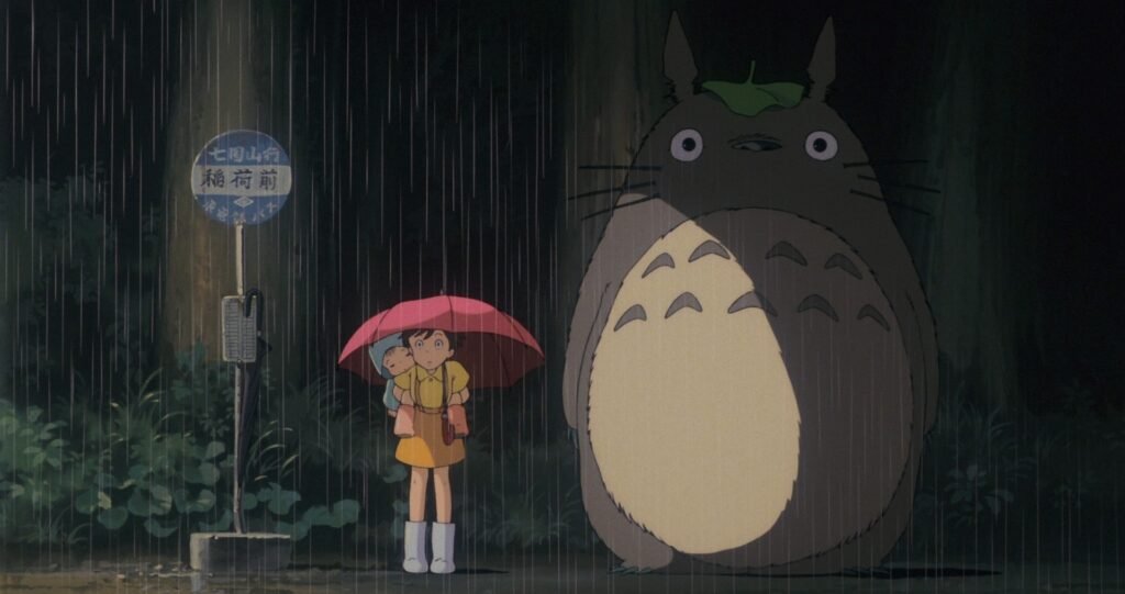 Mei, Satsuki y Totoro bajo la lluvia en la parada del bús